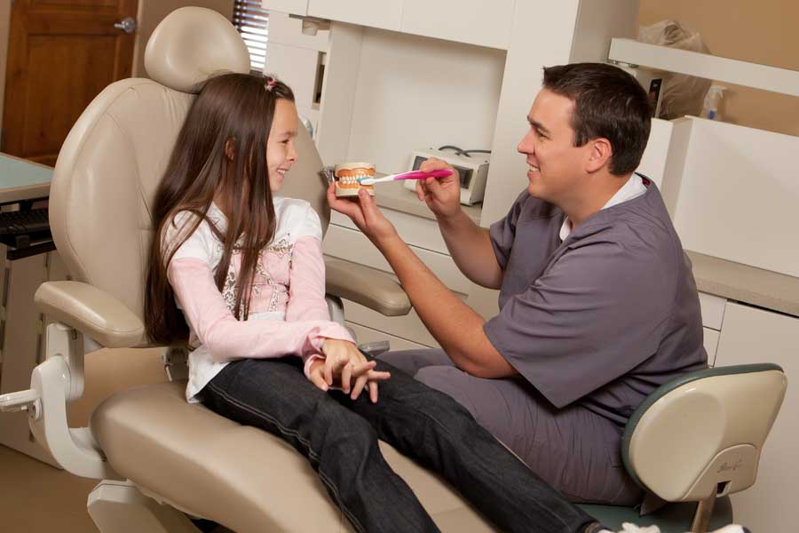 Dentist showing a young patient a tooth model and toothbrush